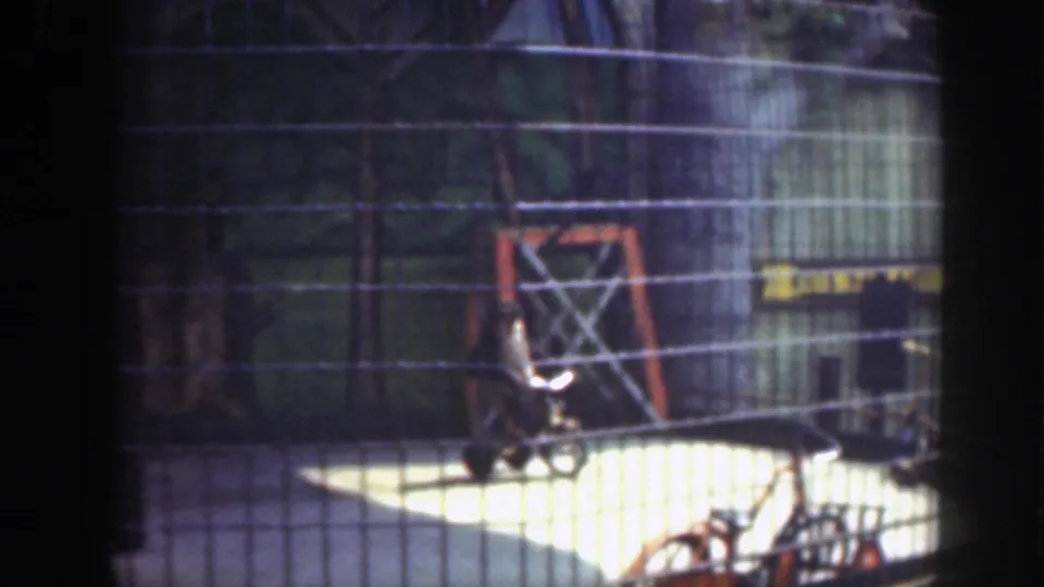 A child rides a bicycle in a fenced Washington, DC outdoor area, with an orange play frame and strong sunlight on the pavement.