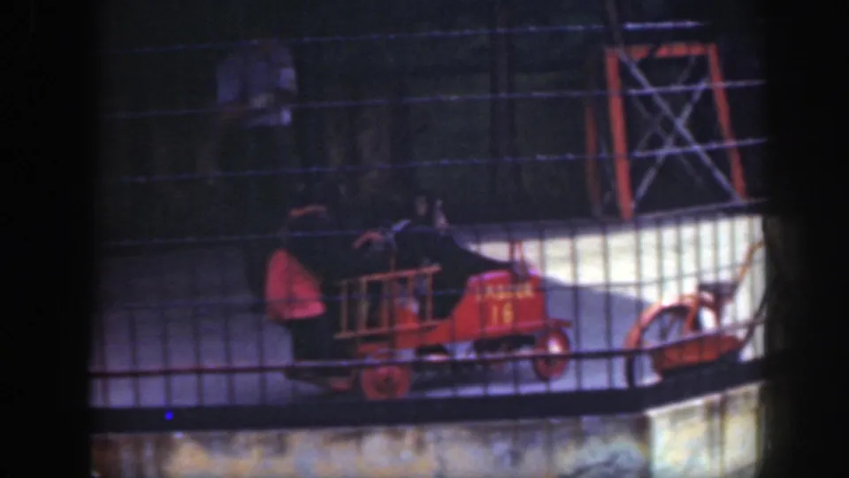 The 1948 Washington DC zoo scene shows chimpanzees on a small red fire truck viewed through heavy wire fencing.