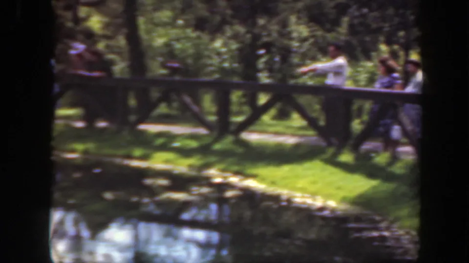 1948 Washington DC park frame showing people near a wooden fence, a pond edge, grass, trees, and bright reflected water.