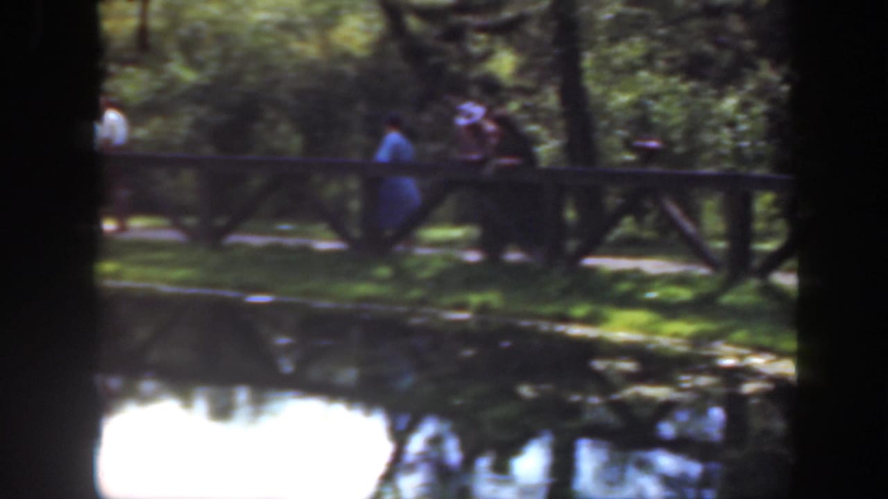 In 1948 Washington, DC home-movie footage, visitors gather along a wooden fence near a reflective pond under tree shade.