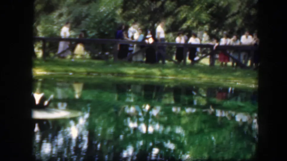 Soft 8mm frame from Washington, DC in 1948 showing adults gathered by a bridge and pond in a leafy park setting.