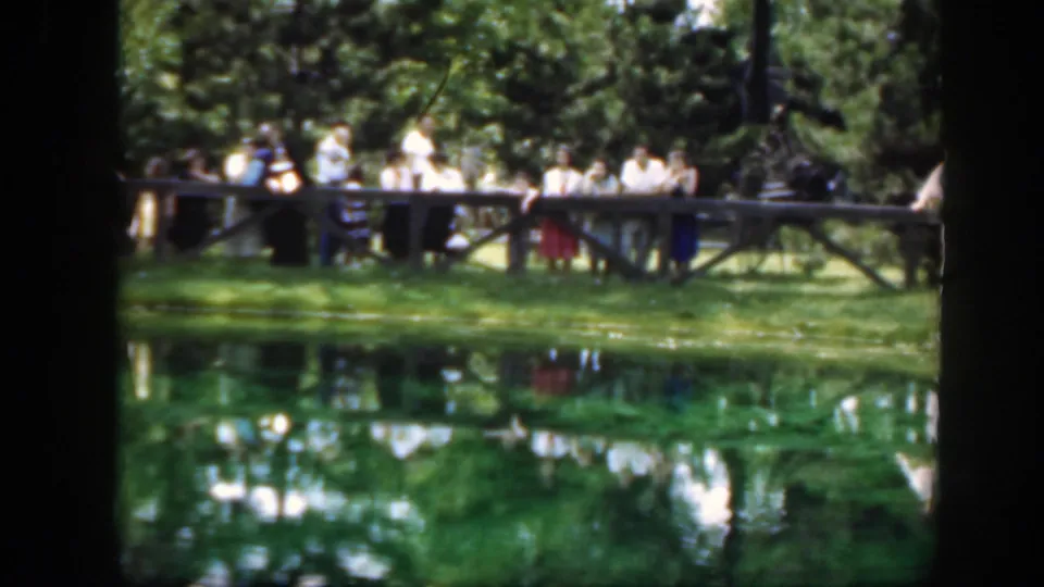 1948 Washington, DC home-movie frame showing a larger group along a wooden bridge next to a reflective pond and trees.