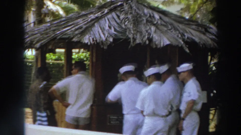 Thatched-roof resort hut in Puerto Rico with men in white uniforms and nearby visitors on a shaded tropical walkway.