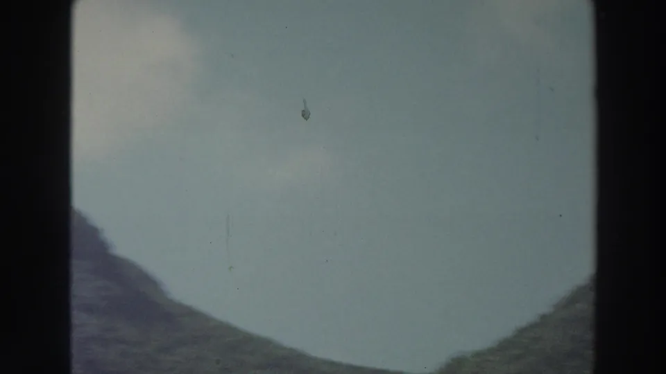 1966 Puerto Rico 8mm frame with distant mountain slopes, pale sky, and sparse visible foliage near the lower frame edge.
