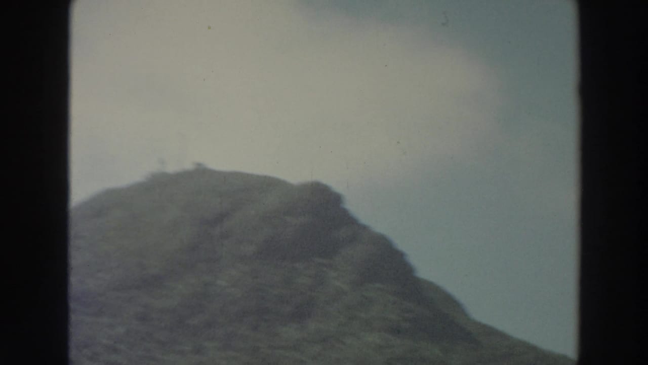 Tree-covered hill rising below a pale blue sky with dark 8mm frame edges.