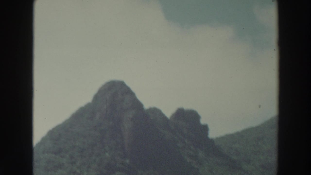 1966 Puerto Rico 8mm view of a distant, rugged wooded ridge under thin white clouds and faded color.