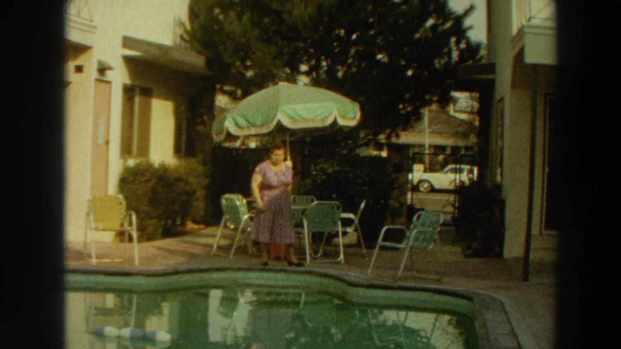 Woman in a purple dress standing beside a motel swimming pool and patio umbrella.