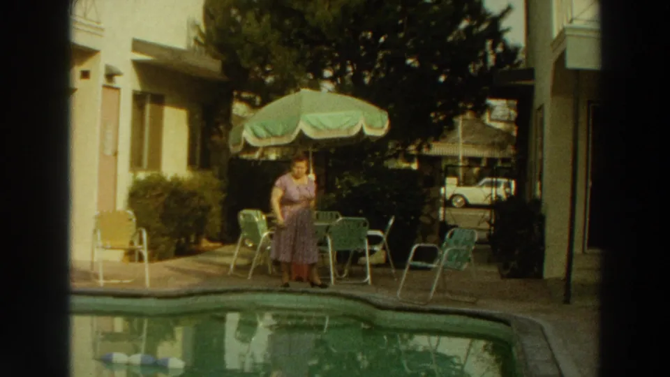 1966 Puerto Rico poolside home-movie frame with a woman in a purple dress near a green-and-white umbrella, chairs, and a parked white car.