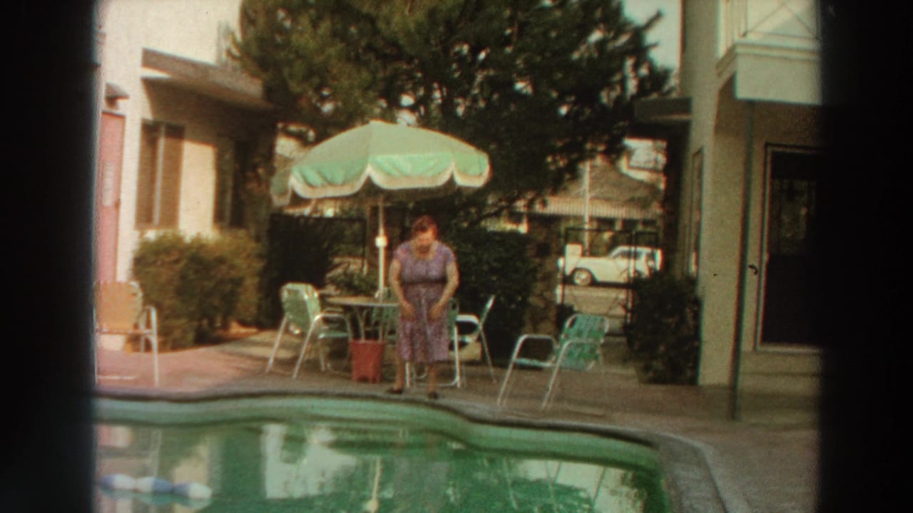 In 1966 Puerto Rico home-movie footage, a woman stands at the pool edge beside patio furniture and a green umbrella.