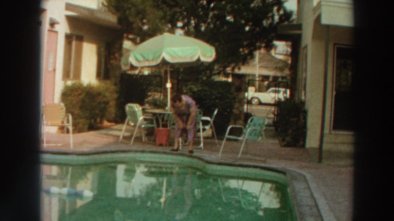 The woman bends at the pool edge in 1966 Puerto Rico footage, with a patio umbrella, chairs, and car in the background.