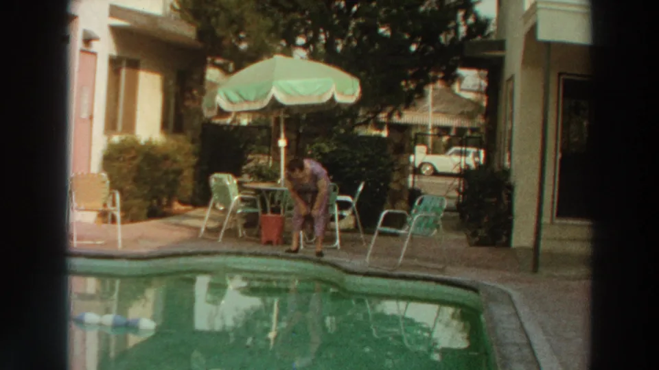 The woman bends at the pool edge in 1966 Puerto Rico footage, with a patio umbrella, chairs, and car in the background.