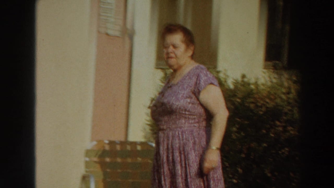 A woman in a purple patterned dress walks past a sunlit building exterior in Puerto Rico, with shrubs and poolside furniture nearby.