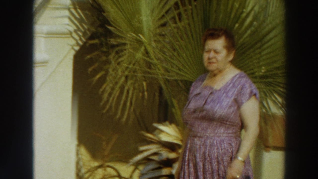 In Puerto Rico home-movie footage from 1966, a woman in a lilac patterned dress stands beside palm fronds in bright sun.