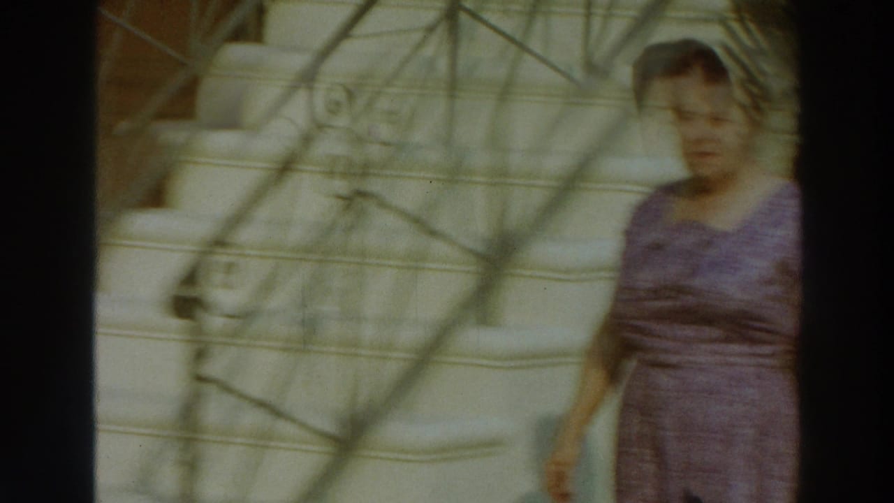 The woman walks past a white staircase and ornate metal railings in 1966 Puerto Rico home-movie footage.