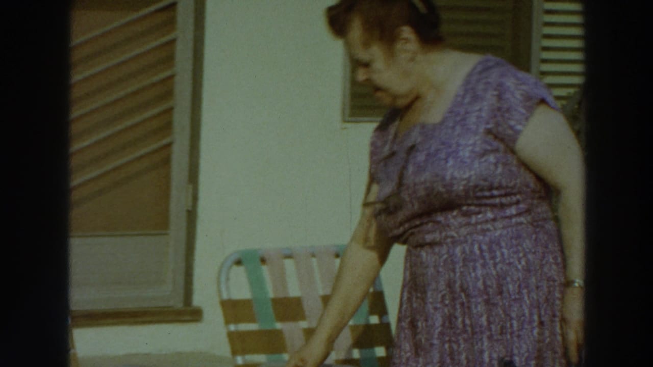 In 1966 Puerto Rico home-movie footage, a woman in a purple dress moves past striped patio chairs outside a building.