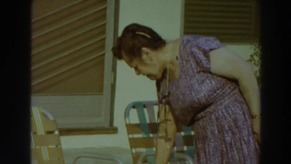 A woman in a purple patterned dress bends beside outdoor chairs on a sunny Puerto Rico patio in 1966 footage.