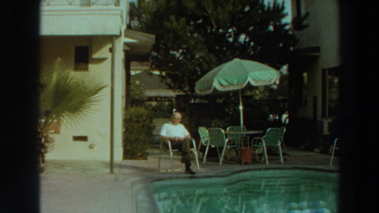 A man in a white shirt sits by a pool near green patio furniture and a green umbrella in 1966 Puerto Rico footage.