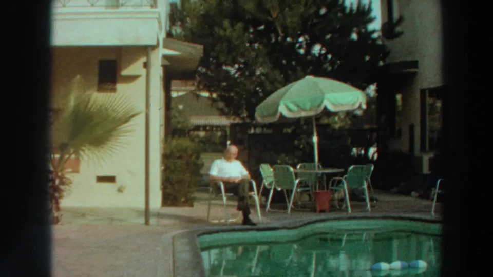In this Puerto Rico 1966 home-movie frame, a seated man is shown by the pool with green patio furniture and a potted palm nearby.