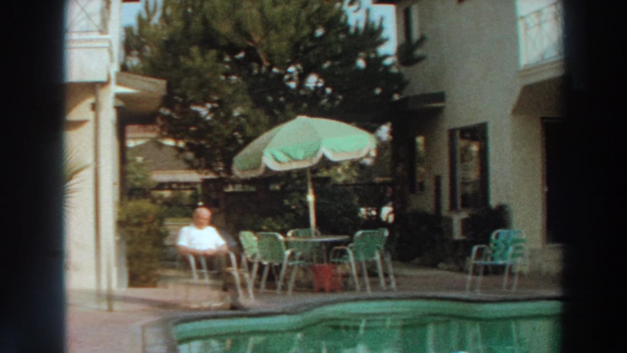 Home-movie view of an elderly man relaxing beside a pool in Puerto Rico, framed by dark film-gate edges.