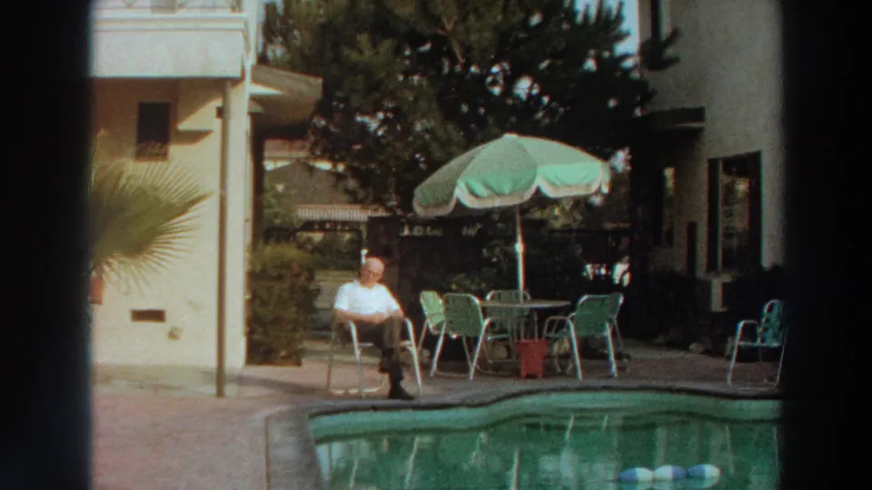 1966 Puerto Rico home-movie frame of a quiet backyard pool area with a seated man and shaded patio furniture.