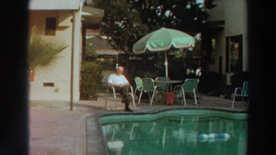 1966 Puerto Rico frame showing a man alone by a backyard pool, with green patio furniture and residential surroundings.