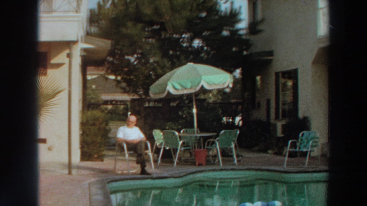 Poolside patio with seated man, parasol, chairs and residential exterior.