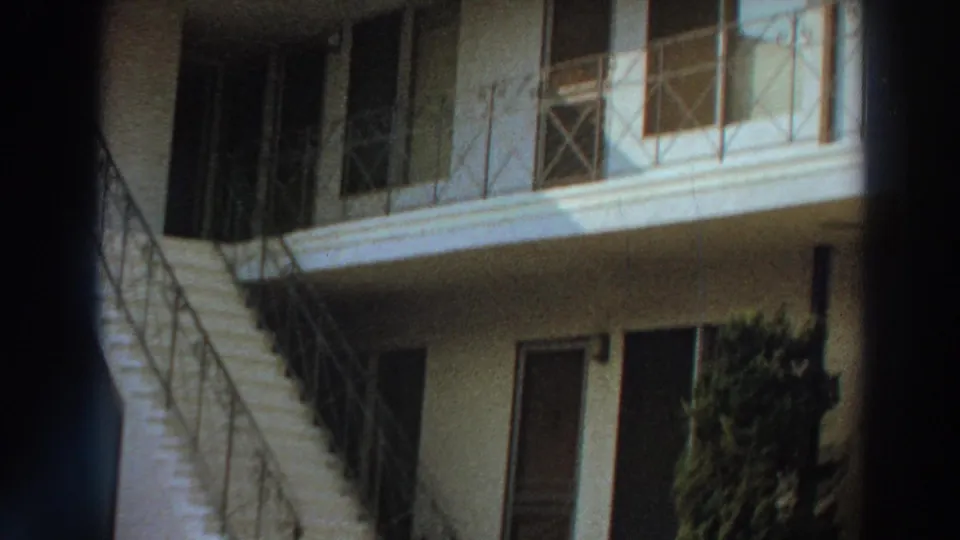 1966 Puerto Rico 8mm frame showing the camera pan toward an exterior staircase, balcony railings and shaded apartment doors.