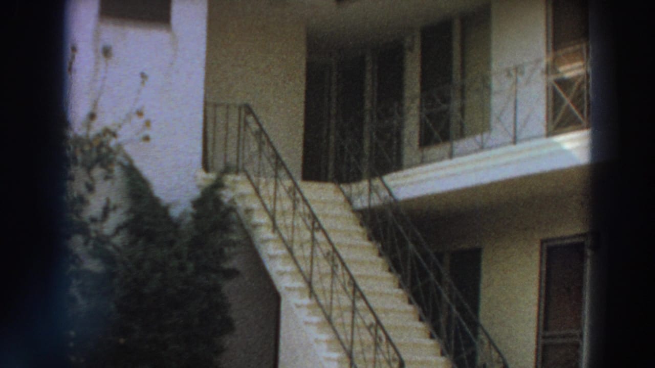 White stucco building with exterior stairs, metal railings, plants, and dark vertical film edge.