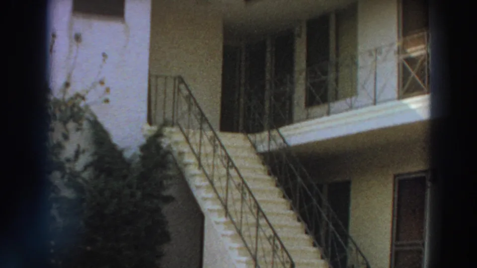 1966 Puerto Rico 8mm frame showing a stucco courtyard building with exterior stairs, metal railings, and greenery.