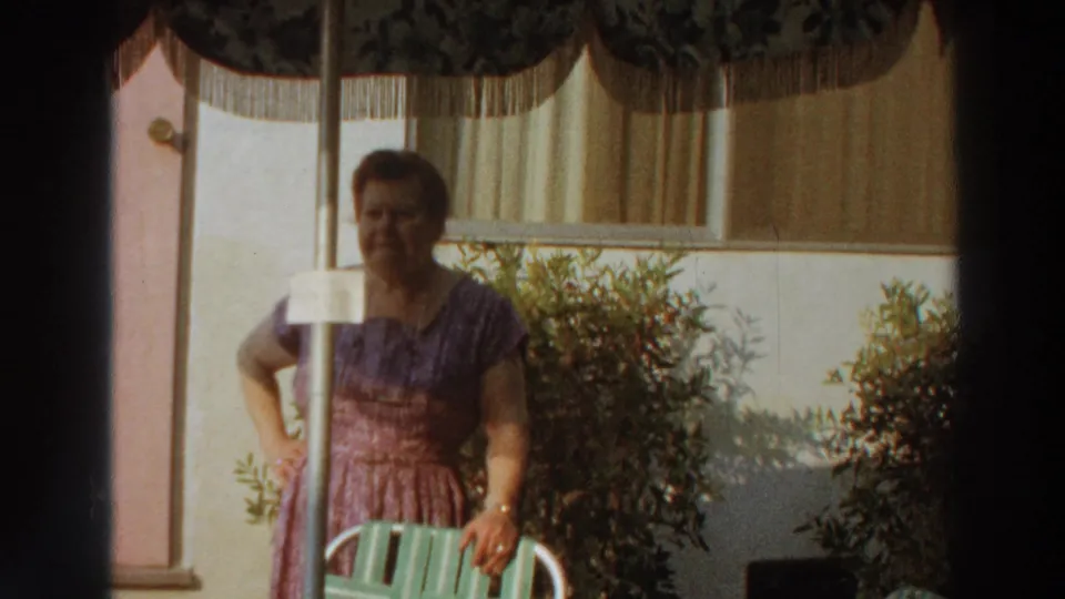 1966 Puerto Rico home-movie frame of an adult woman in a purple dress standing by a poolside chair.
