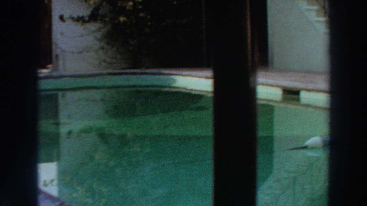 1966 Puerto Rico home-movie frame with green pool water, pale coping, nearby deck, and dark window bars in the foreground.