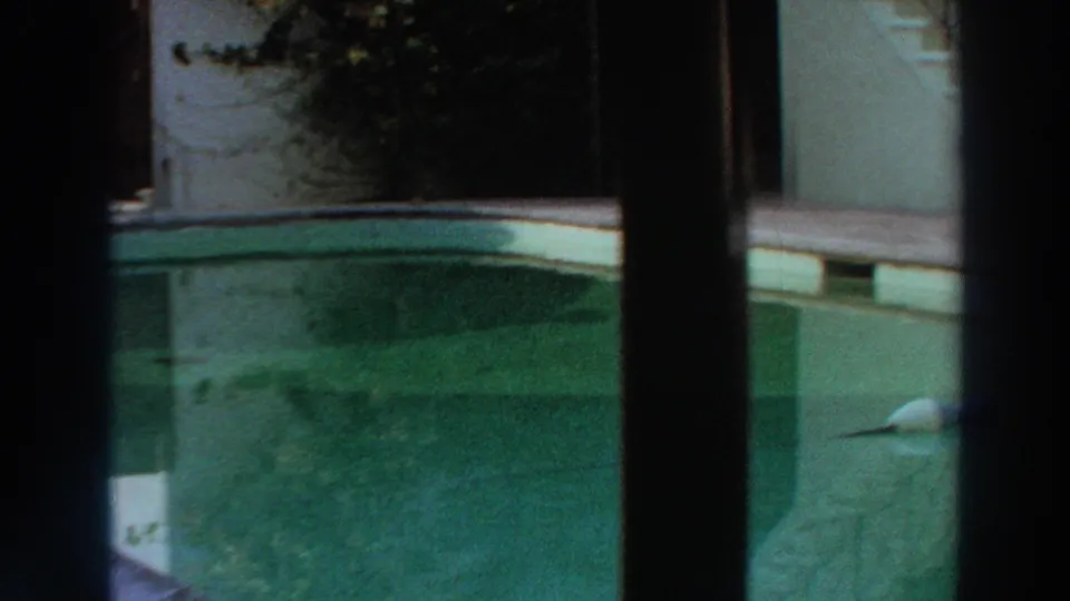 1966 Puerto Rico home-movie frame with green pool water, pale coping, nearby deck, and dark window bars in the foreground.