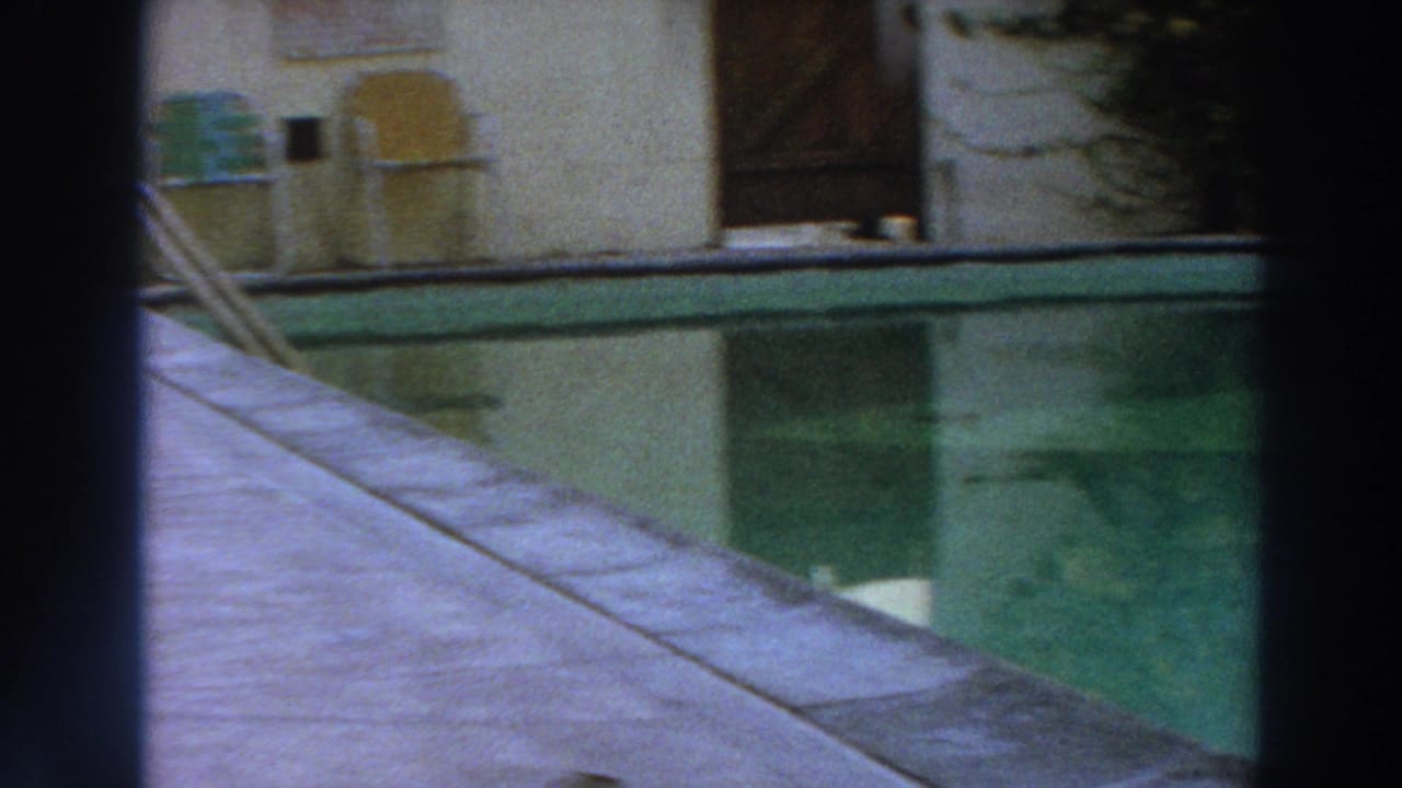 1966 Puerto Rico 8mm frame showing a pool ladder, concrete deck, doorway, wall fixtures, and green pool water through dark bars.