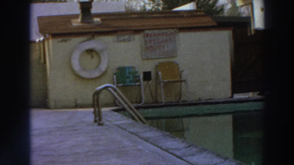 1966 Puerto Rico frame showing a poolside warning sign, white life preserver, metal chairs, ladder, and green pool edge.