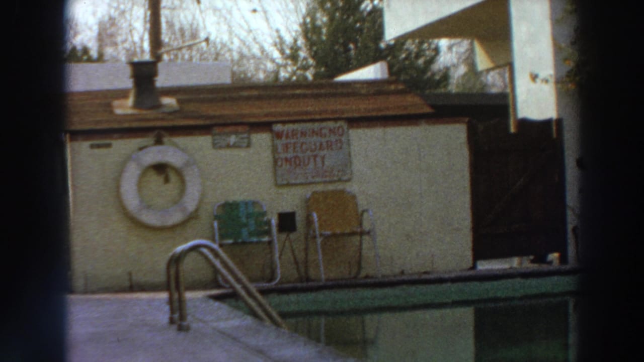 1966 Puerto Rico home-movie frame showing a poolside hut with a life ring, chairs, a warning sign, and the edge of a swimming pool.