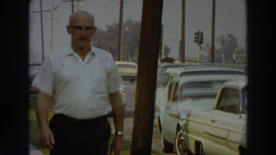 1966 Puerto Rico street view with a man walking on the sidewalk past parked cars, utility poles, and traffic signals.