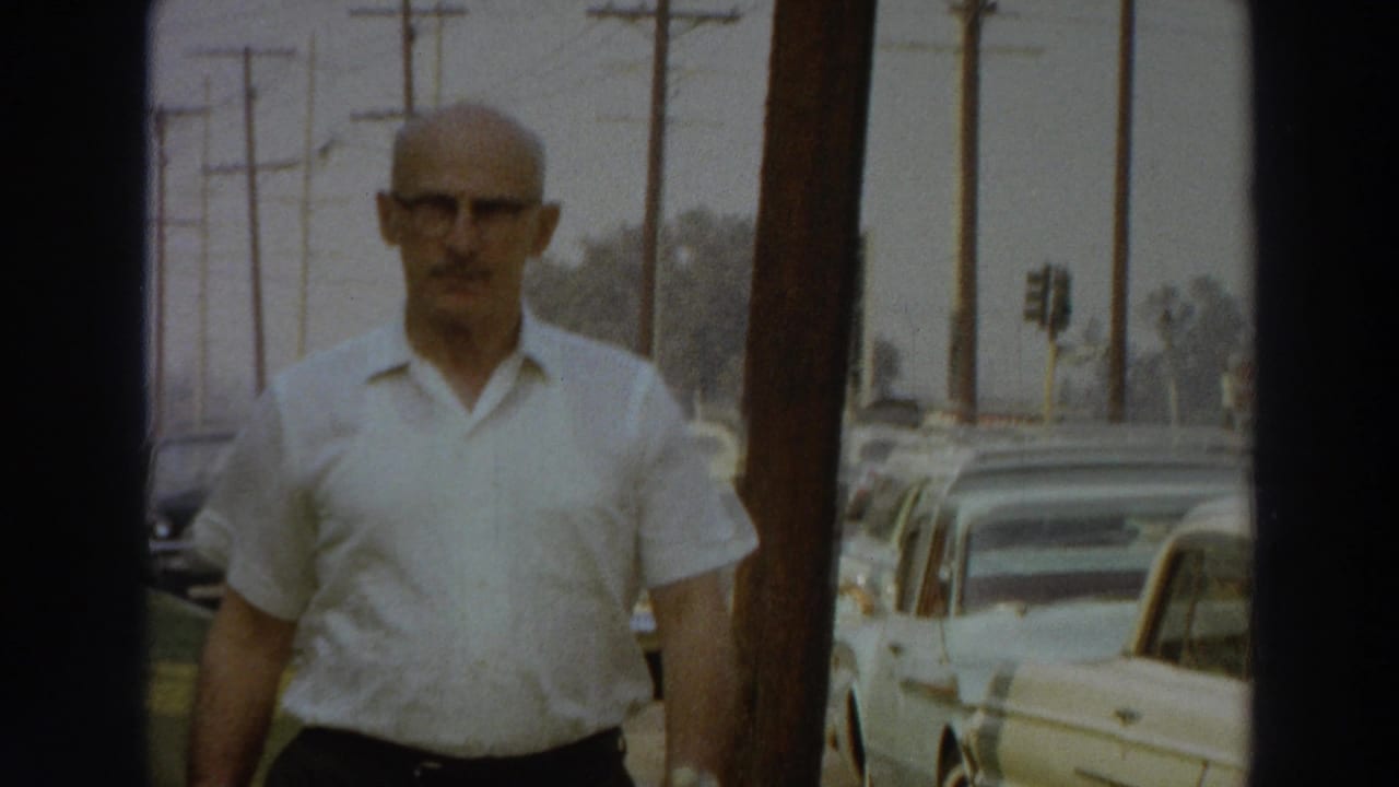 Close 8mm view of the man in a white shirt and dark trousers walking along a Puerto Rico sidewalk in 1966.