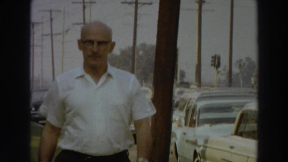 Close 8mm view of the man in a white shirt and dark trousers walking along a Puerto Rico sidewalk in 1966.