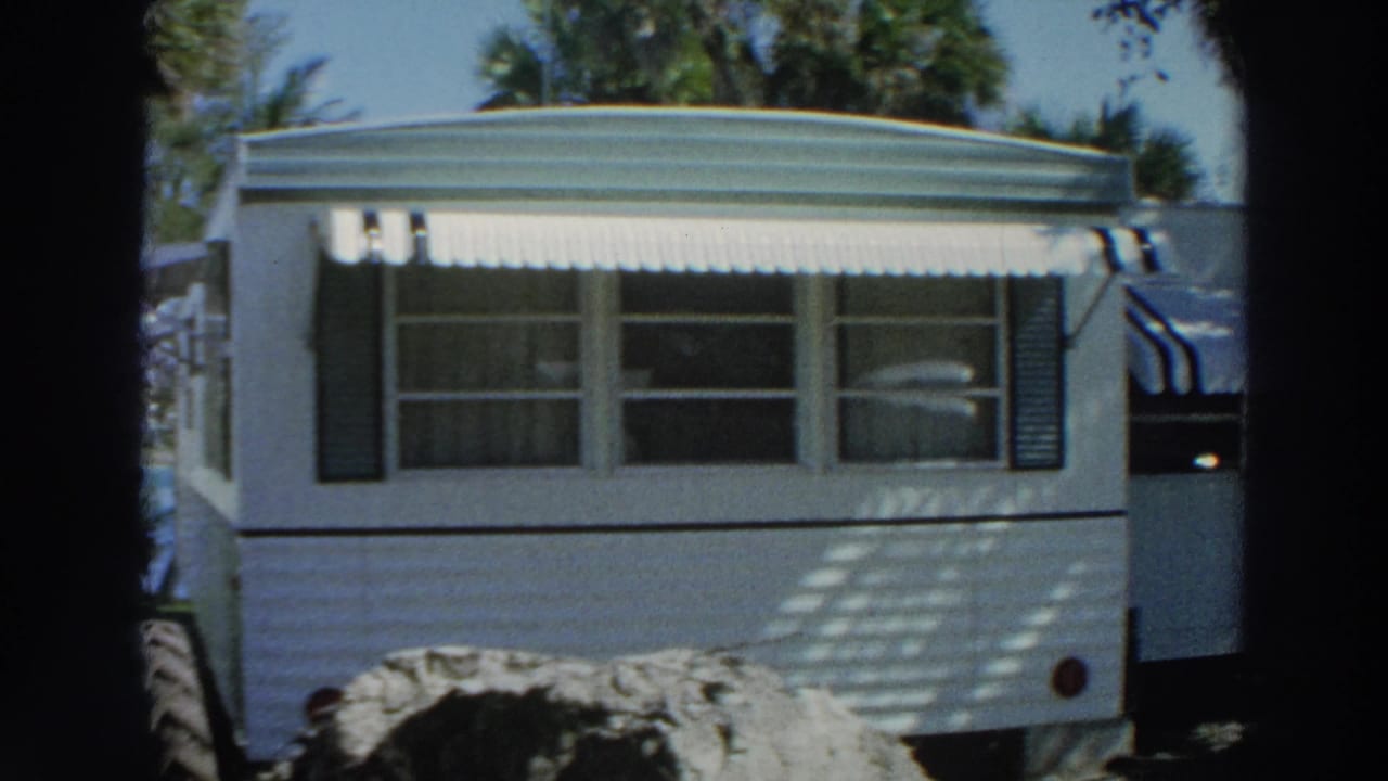 1966 Puerto Rico 8mm frame showing a white mobile home trailer with striped awning, windows, and palm trees in bright sun.
