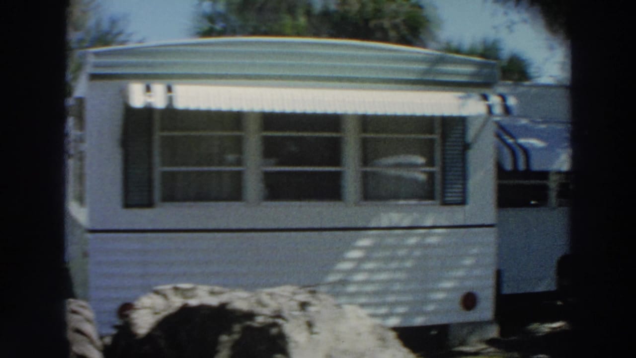 1966 Puerto Rico frame of a white mobile home trailer with awning, shutters, windows, and a large tire visible near the side.