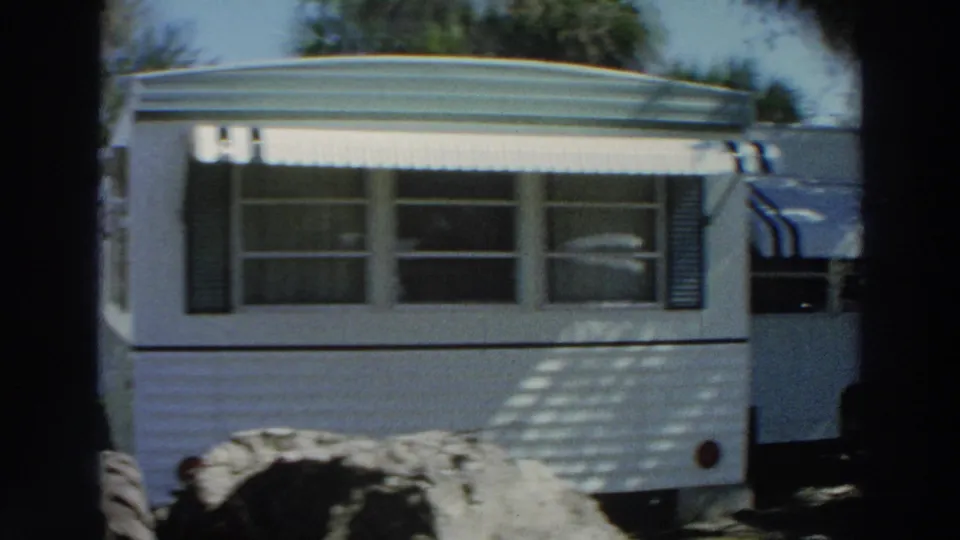 1966 Puerto Rico frame of a white mobile home trailer with awning, shutters, windows, and a large tire visible near the side.