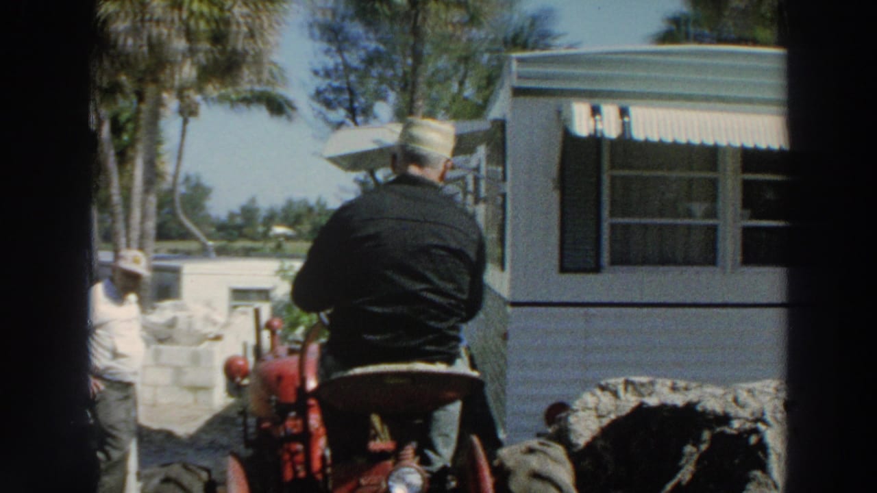 1966 Puerto Rico home-movie frame showing a man from behind on a red tractor beside a white trailer and another worker nearby.