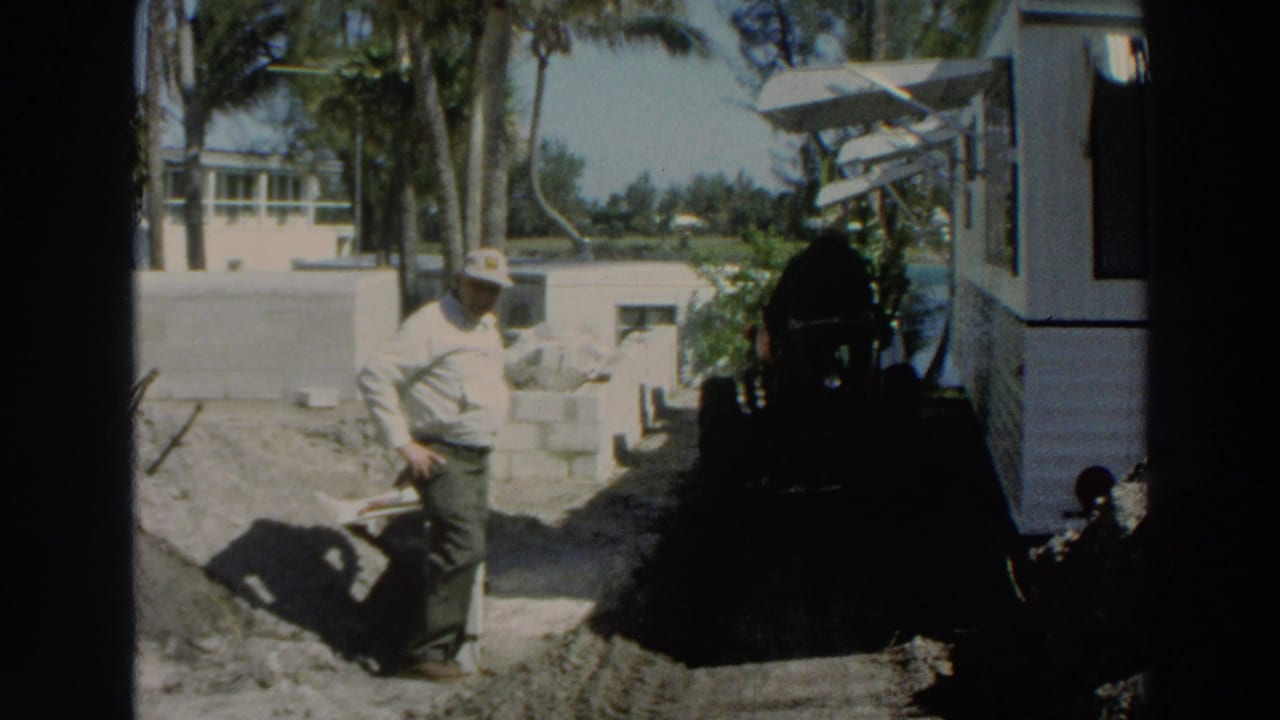 Man stands beside concrete blocks with a dark machine or equipment shape nearby.