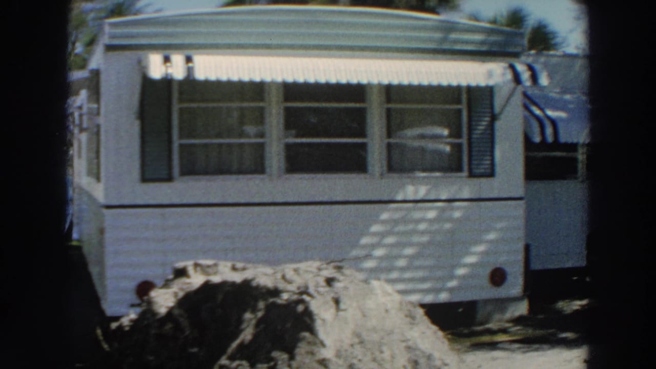 1966 Puerto Rico 8mm frame showing a white mobile home, striped awning, shaded driveway, and dark parked sedan.