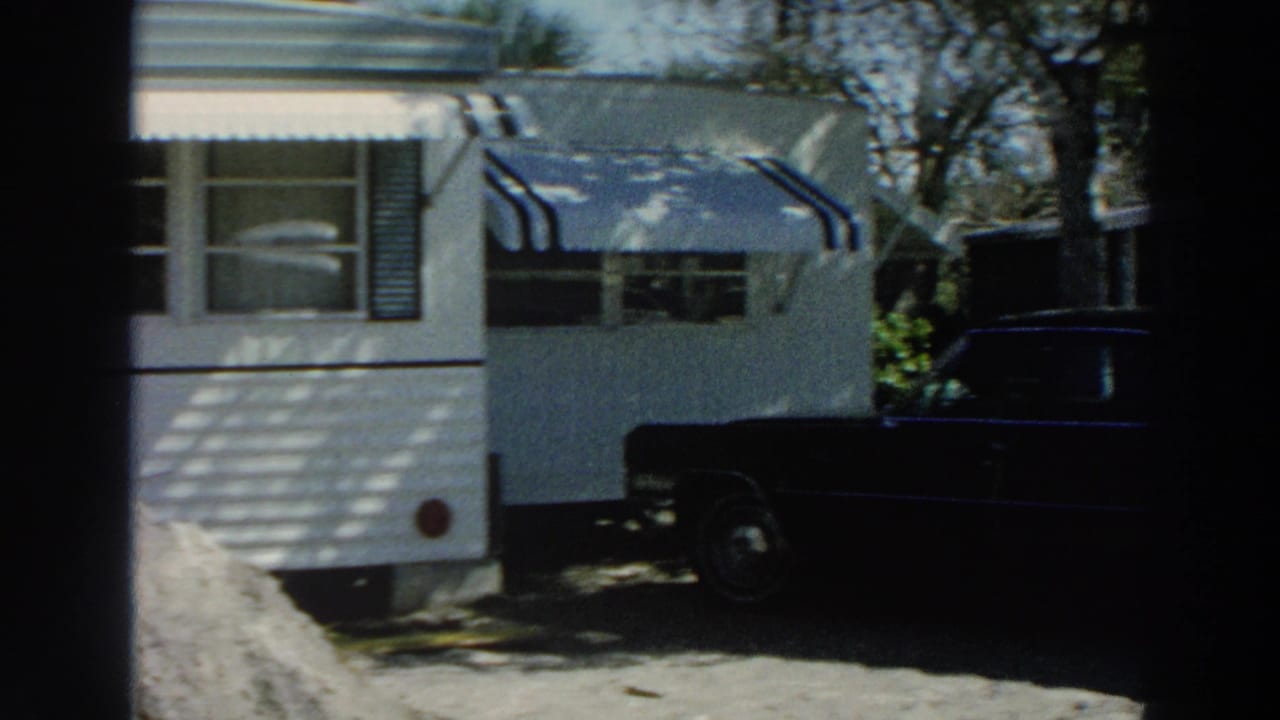 White trailer with striped awnings and a dark car parked nearby in a bright Puerto Rico trailer park scene.