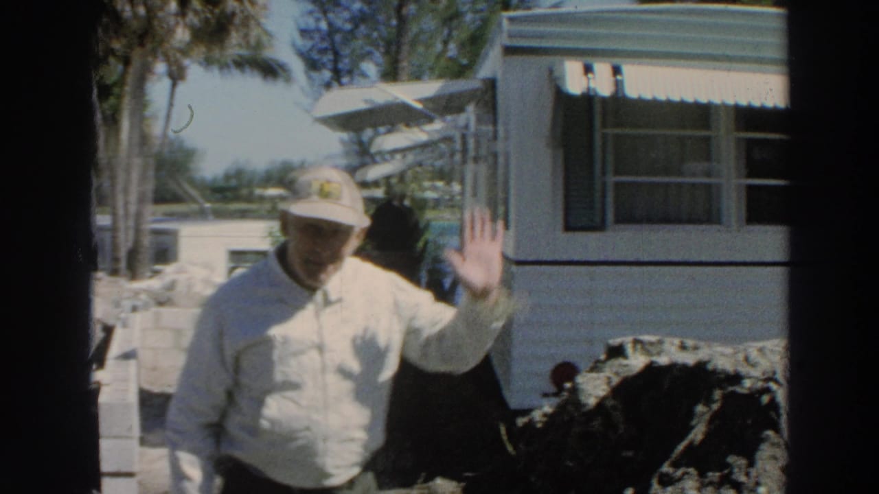 1966 Puerto Rico home-movie frame of an adult man in a light shirt and cap waving near a white mobile home.