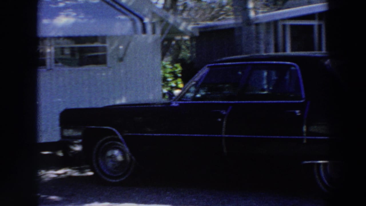 Dark sedan parked beside a white mobile home in strong shade.