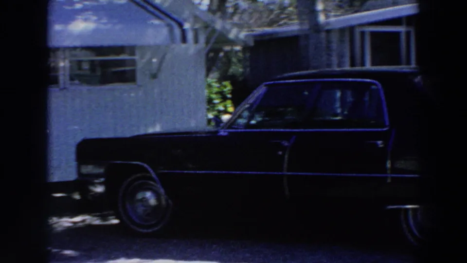 1966 Puerto Rico 8mm frame showing a dark sedan parked next to a white mobile home with awnings and tree shade.