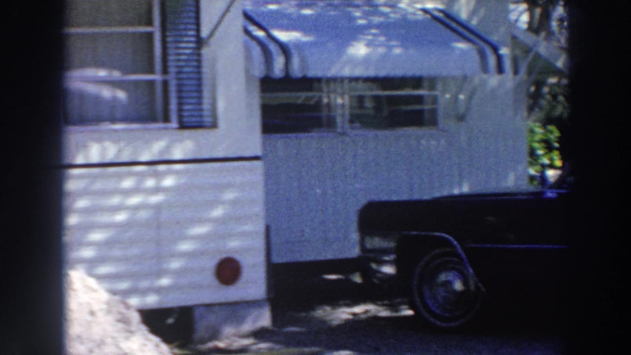 White mobile home exterior in Puerto Rico, 1966, with shaded windows, awnings, and the front of a dark sedan at the edge.
