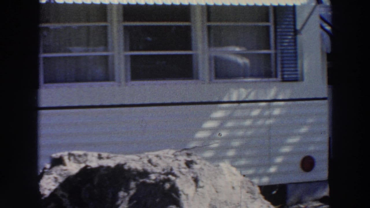 1966 Puerto Rico home-movie frame showing the side of a white mobile home with windows, shutters, and mottled sunlight.